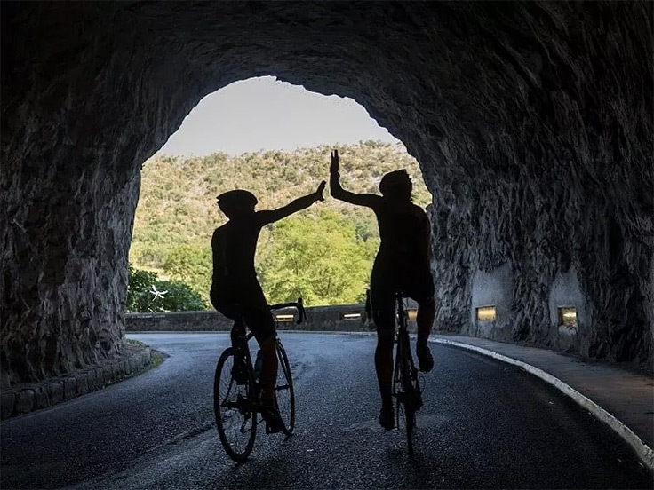 Dans un tunnel, deux cyclistes se font un check pour signifier leur exploit sportif, aux environs du camping 3 étoiles avec piscine Le Petit Pyrénéen en Ariège, dans les Pyrénées
