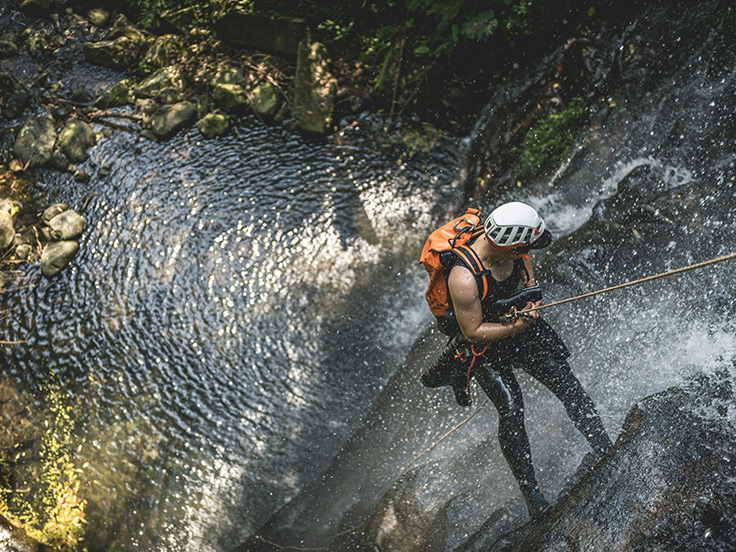 Vue plongeante sur une personne descendant en rappel une cascade dans le cadre d'une session de canyoning, aux alentours du terrain de camping 3 étoiles avec piscine Le Petit Pyrénéen en Ariège, dans les Pyrénées