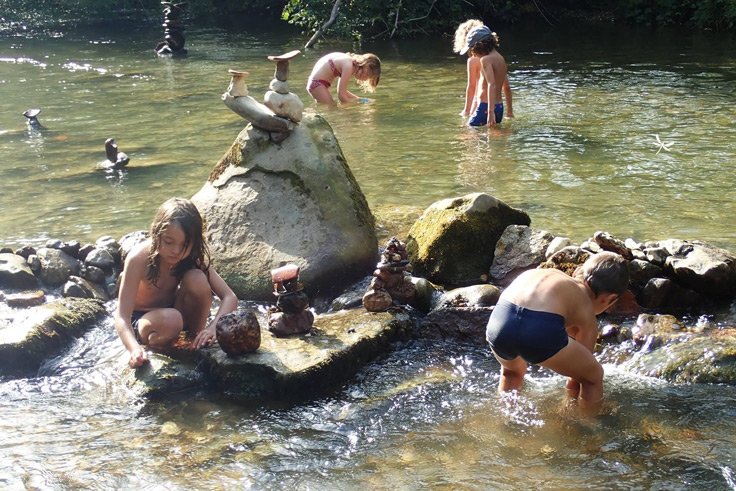 Des enfants jouent avec l'eau de la rivière Arize au bord du terrain de camping 3 étoiles avec piscine Le Petit Pyrénéen en Ariège dans les Pyrénées
