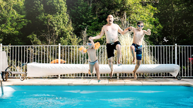 Un père et ses enfants s'amusent à sauter dans la piscine du terrain de camping 3 étoiles avec piscine Le Petit Pyrénéen en Ariège dans les Pyrénées