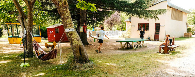 L'aire de jeux pour les enfants avec un trampoline, une table de ping-pong, un hamac, des agrès de sport, etc, au milieu terrain de du camping 3 étoiles avec piscine Le Petit Pyrénéen en Ariège dans les Pyrénées